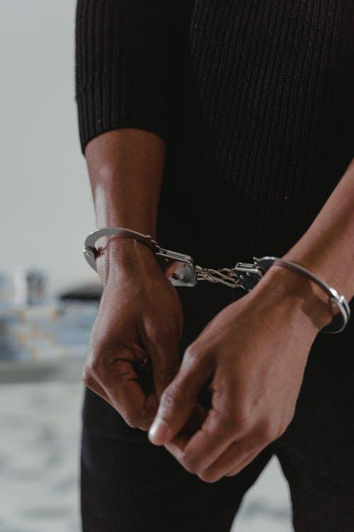 A close-up photo of a person in black clothes in handcuffs