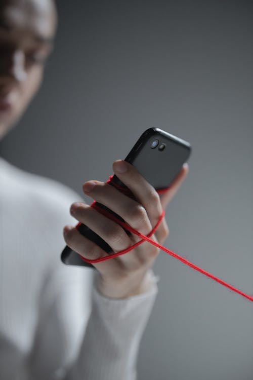 Hand holding a phone with a red thread wrapped around the hand.